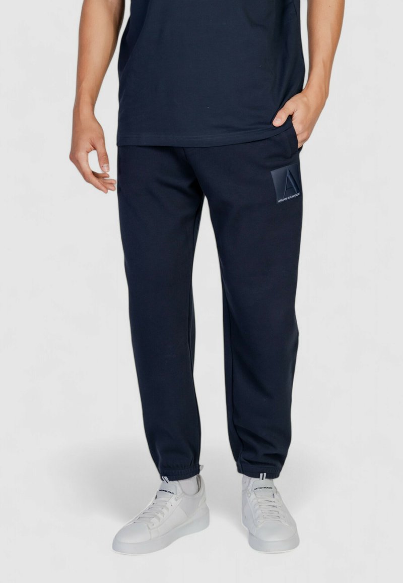 Pantaloni jogger blu navy realizzati in tessuto morbido con polsini elastici, dotati di una piccola etichetta del logo sulla coscia sinistra e tasche laterali.