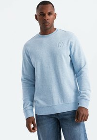 Sudadera azul clara de tejido suave con cuello redondo, puños y dobladillo acanalados, que presenta un pequeño logo texturizado en el pecho.