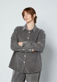 Szara koszula z kordurojki z kołnierzykiem, zapinana na guziki z przodu, o luźnym fasonie. Posiada strukturę prążkowaną oraz długie rękawy z guzikami przy mankietach.