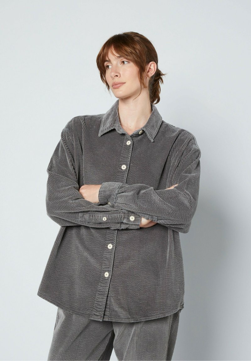 Szara koszula z kordurojki z kołnierzykiem, zapinana na guziki z przodu, o luźnym fasonie. Posiada strukturę prążkowaną oraz długie rękawy z guzikami przy mankietach.