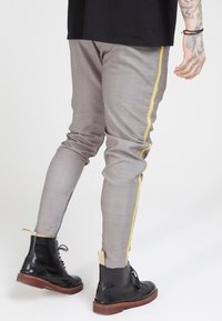 Slim-fit grijze broek met een textuuropervlak, voorzien van een gele streep langs de zijkant, gecombineerd met zwarte veterlaarzen.