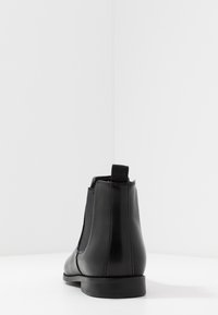 Bottine noire en cuir avec panneau latéral élastique, bout arrondi, languette de tirage et talon bas. Texture lisse et design minimaliste.