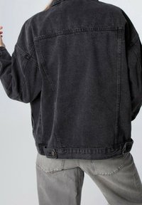 Giacca di jeans nera oversize con un taglio classico, dotata di vita con bottoni, cuciture dettagliate e una stoffa leggermente testurizzata.