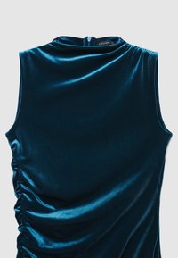 Ärmelloses Oberteil aus samtigem Petrol mit hohem Kragen, seitlicher Raffung und Reißverschluss auf der Rückseite. Glatte, weiche Textur.