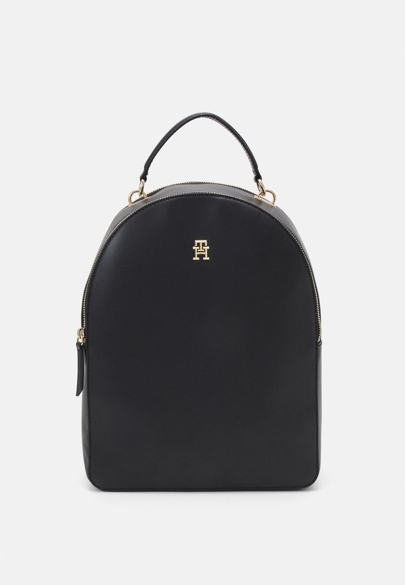 Sac à dos en cuir noir de forme arrondie, avec quincaillerie dorée et un logo sur le devant. Il dispose d'une poignée supérieure et d'une fermeture éclair.