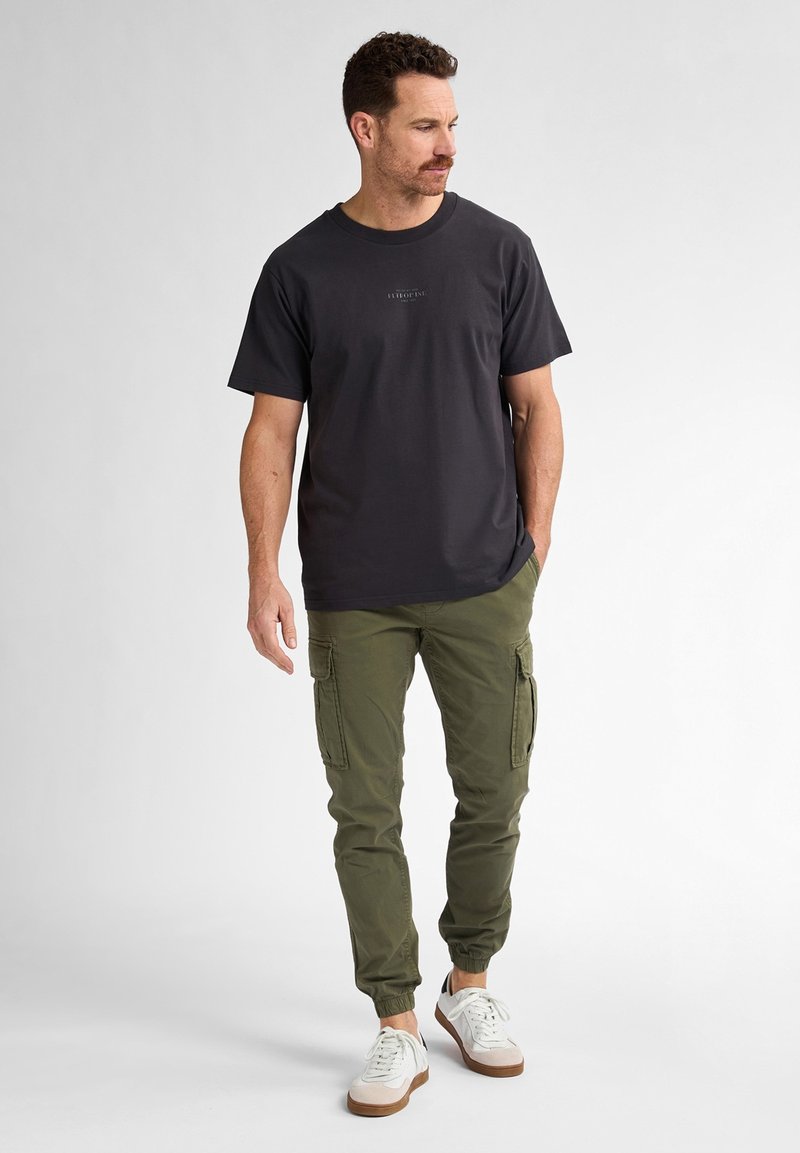 Mørkegrå bomulds T-shirt med rund hals, parret med olivengrønne cargo bukser med flere sidelommer, og hvide sneakers.