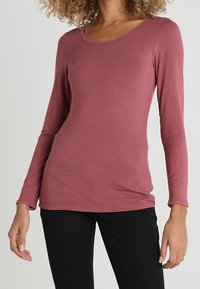 Långärmad topp i dämpad ros, tillverkad av mjukt tyg. Den har en scallop-krage och manschetter, designad för en figurnära silhuett.