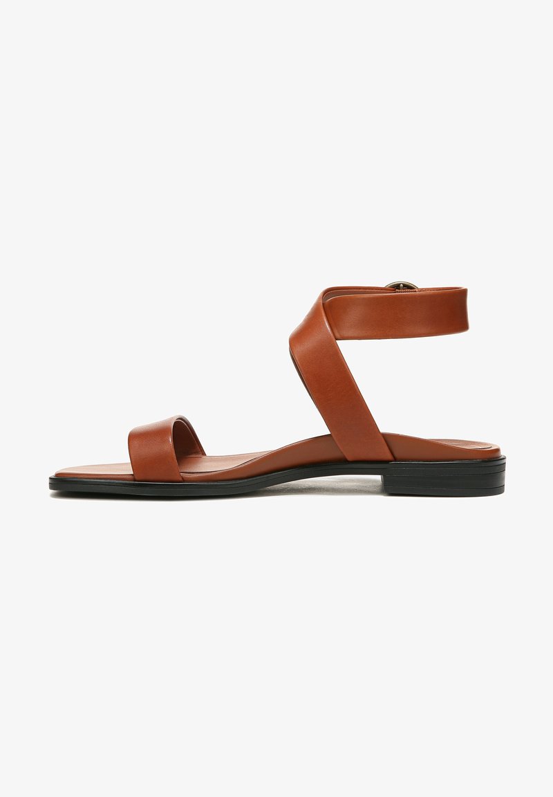Brown leather flat sandal with ankle strap and open toe, featuring a black sole and low heel.