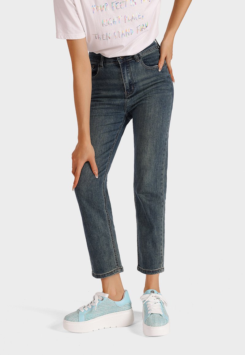 Jeans a vita alta, blu scuro, con un taglio dritto; indossati con sneaker platform azzurri chiari con dettagli testurizzati e accenti bianchi.