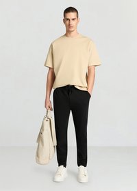 Beige short-sleeve shirt with a loose fit, paired with black tapered pants featuring an elastic waist and side pockets. The model holds a cream bag.