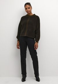 Pull marron avec des rayures diagonales noires, encolure ronde et manches ballons. Associé à un pantalon noir à jambes droites et des bottines.