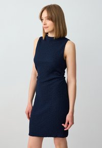 Navy blue dress with a textured fabric, sleeveless design, high neckline, and a gathered side detail for a fitted silhouette.