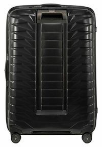 Valise rigide noire avec un extérieur texturé et strié, dotée d'une poignée rétractable et de quatre roues pour faciliter le déplacement.