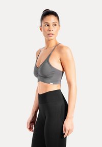 Grijze sportcrop top met ruches, dunne schouderbandjes en een rekbare pasvorm, gecombineerd met zwarte leggings met hoge taille.