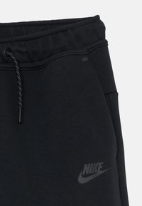 Melni kokvilnas sporta bikses ar teksturētu vidukļa jostu un auklu, kā arī mazu, tumšu Nike logotipu kreisajā augšstilbā.