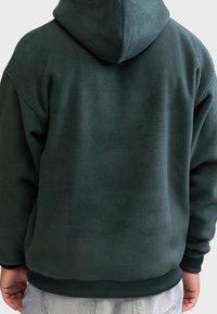 Mørkegrøn fleece hættetrøje med en stor hætte, ribbede manchetter og kant. Blød tekstur med en afslappet pasform. Ingen synlige mønstre eller accenter.