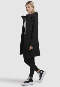 Black hooded coat with a zippered front and long sleeves, paired with black leggings and high-top black and white sneakers.