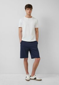 T-shirt blanc à manches courtes, short rayé bleu et baskets blanches avec des accents foncés. Tenue décontractée avec une coupe relax et des poches.