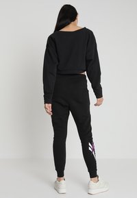 Sudadera negra corta de manga larga, combinada con pantalones deportivos negros que tienen un gráfico en blanco y morado en la pierna. Zapatillas blancas.