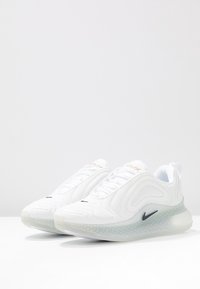 Paire de baskets blanches Nike Air Max avec semelle translucide à pois et logo swoosh noir, présentée côte à côte sur une surface blanche.