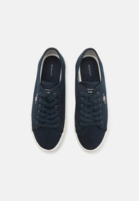 Marineblaue Segeltuch-Sneaker mit weißen Gummisohlen, runder Zehenform, sechs Ösen mit Schnürsenkeln und einem kleinen gestickten Logo an der Seite.