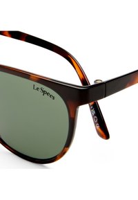 Γυαλιά ηλίου με ταρταρούγα και σκούρους πράσινους φακούς με το λογότυπο «Le Specs» στην επάνω αριστερή γωνία του φακού.