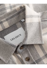 Szara i kremowa koszula flanelowa w kratę z klasycznym kołnierzykiem, dwoma brązowymi guzikami oraz metką z napisem "LES DEUX" i rozmiarem "M".