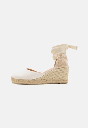 Espadrille compensée beige avec empeigne texturée, semelle en jute et lacets à nouer autour de la cheville. Présente une finition lisse et un bout arrondi.