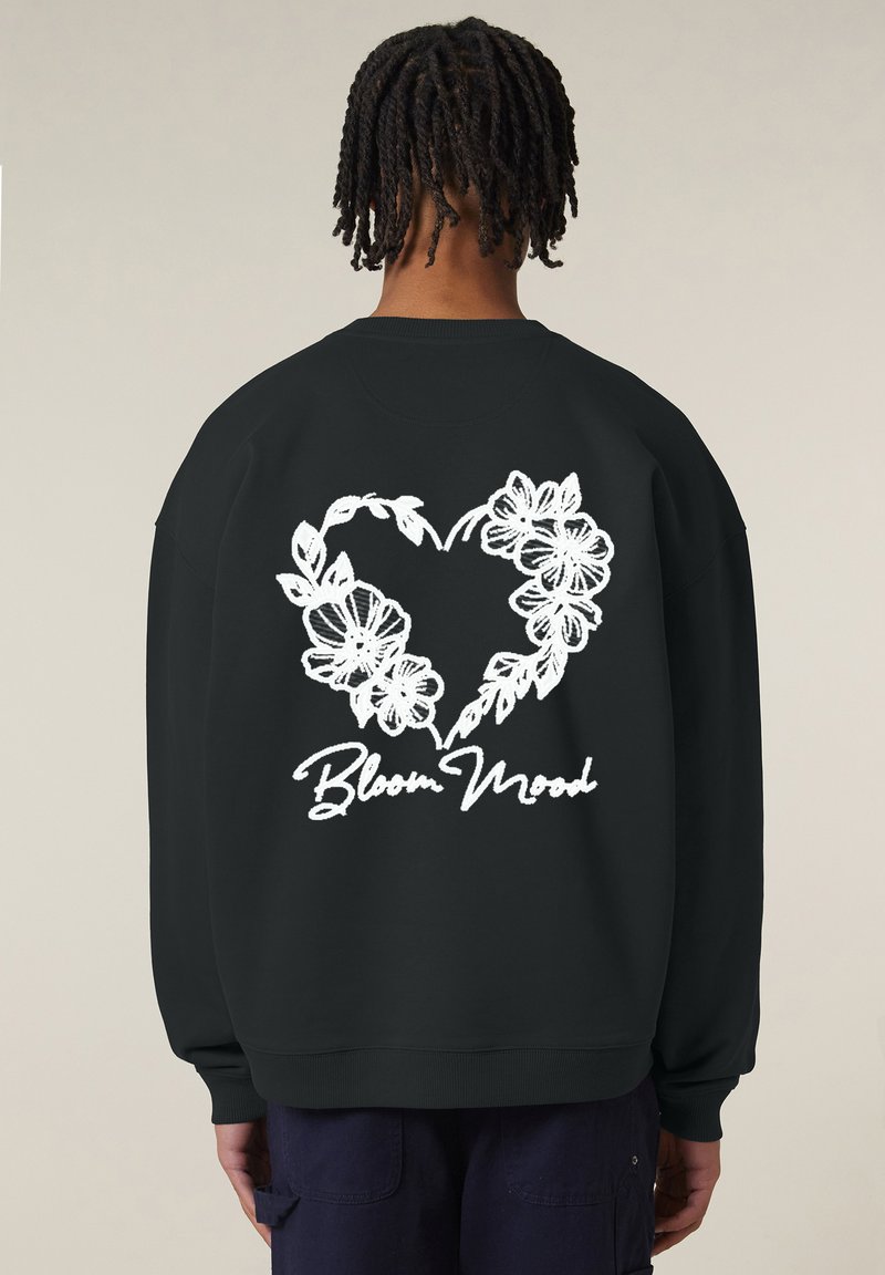Felpa nera con un design a forma di cuore floreale bianco e il testo "Bloom Mood" sotto. Tessuto morbido, vestibilità comoda, polsini e orlo a coste.