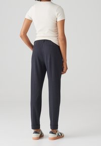 Mörkblå, skräddarsydda byxor med slim fit, uppvikt fåll och bakficka, i kombination med en figurnära krämfärgad ribbad t-shirt och sneakers.