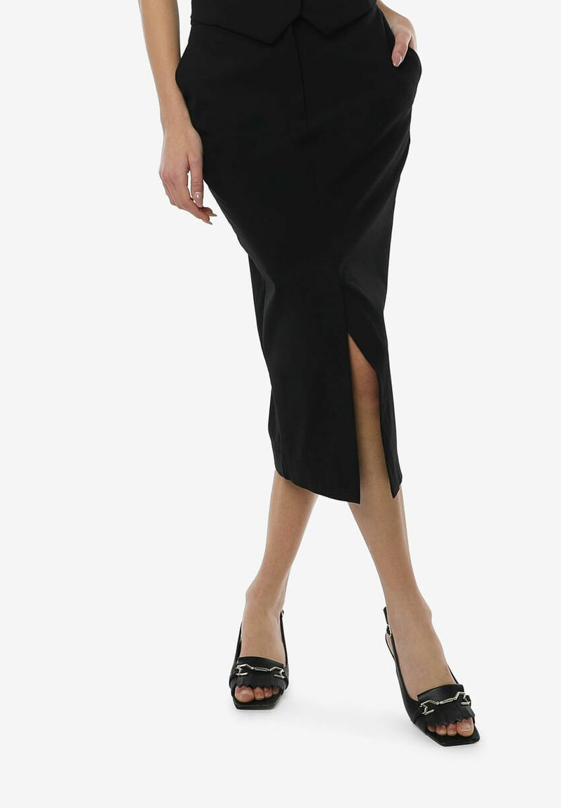 Sorte tætsiddende midiskirt med en frontslids, lavet af glat stof. Båret med sorte slingback hæle med dekorative kædedetaljer.