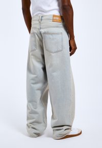 Jasnoniebieskie, oversize'owe dżinsy z wysokim stanem, dwoma tylnymi kieszeniami i brązową metką przy pasie. Gładka tekstura i luźny krój.