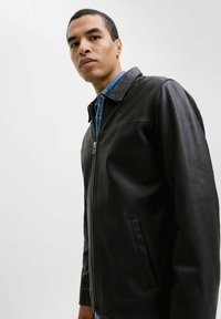 Black leather jacket with a smooth texture, featuring a zip closure, collar, and side pocket. Worn over a blue denim shirt.