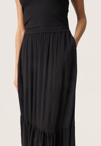 Jupe maxi noire en tissu léger, dotée d'une texture plissée, d'une taille élastique et de poches latérales pour plus de fonctionnalité.