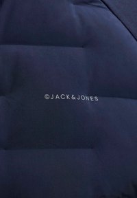 Temno mornarsko modra prešita tkanina z osrednjim belim napisom blagovne znamke "JACK & JONES" na površini.