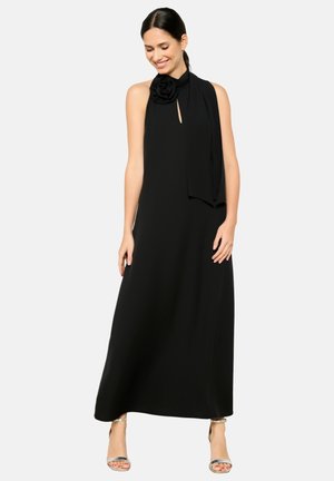 Robe halter noire avec un accent de rose au niveau du décolleté, silhouette fluide et tissu lisse. Associée à des sandales argentées à lanières.