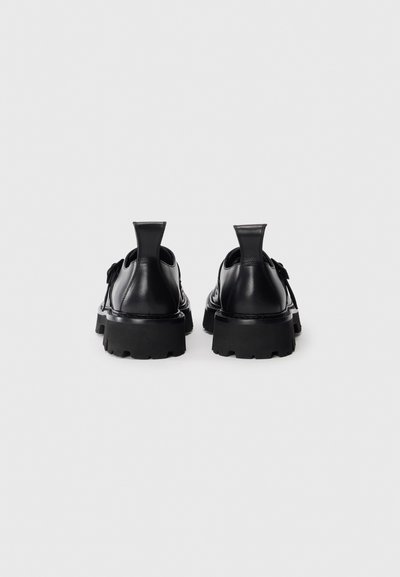 Pantofi din piele neagră cu o talpă groasă, având o textură netedă, cu fante la călcâi și fără modele sau accesorii vizibile.