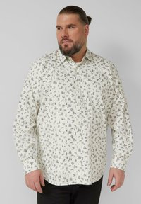 Witte blouse met zwartgedrukte patronen, lange mouwen, kraag met knopen en een losse pasvorm. De stof lijkt lichtgewicht met een gladde textuur.