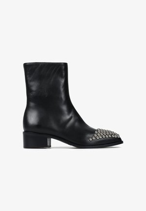 Czarne skórzane botki za kostkę na masywnym obcasie, z ostrym noskiem ozdobionym srebrnymi ćwiekami w skupionej formie. Gładka tekstura.