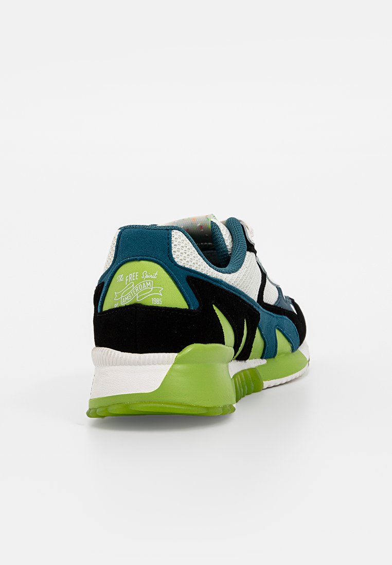 Sneaker mit weißen Mesh, teal, schwarzen und grünen Wildlederpaneelen, grüner Sohle und dem Text "The Free Spirit Amsterdam 1985" an der Ferse.