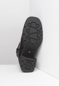 Black leather boot with a rubber sole featuring a textured tread pattern, side zipper closure, and embossed brand logo on the heel.