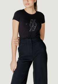 T-shirt nera a maniche corte con design di logo metallico, abbinata a pantaloni neri a vita alta e dalla vestibilità ampia.