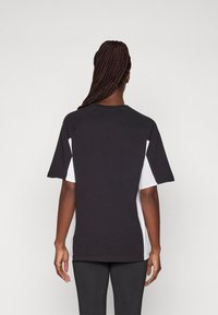 Zwart-witte sportshirt met korte mouwen en raglanmouwen, gemaakt van een gladde stof, met een contrasterend wit zijpaneel.