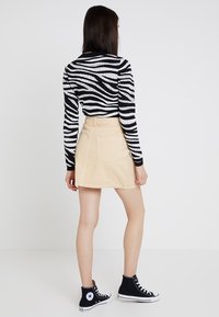 Top de rayas blanco y negro de manga larga, falda de mezclilla beige, zapatillas negras de caña alta. Incluye un diseño ajustado y bolsillos traseros.