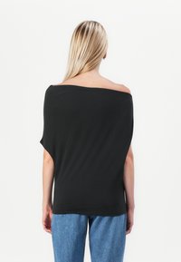 Zwarte off-shoulder top met een losse pasvorm, korte mouwen en een gladde textuur, gecombineerd met lichtblauwe spijkerbroek.