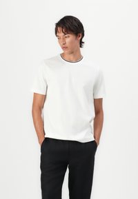 T-shirt bianca a maniche corte con un motivo testurizzato e colletto girocollo a coste nere, abbinata a pantaloni neri larghi.