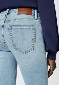 Jeans in denim azzurro con una tasca posteriore che presenta un piccolo logo ricamato e un'etichetta in pelle marrone con la scritta "FINKO DENIM." Texture liscia.