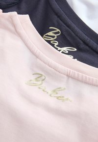 Tuvplāns ar sakrautām rozā un tumši zilām T-kreklām ar zelta burtiem "Baker" pie apaļām apkaklītēm.