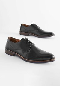 Schwarze Lederschuhe mit glatter Oberfläche, runder Spitze und minimaler Naht. Sie verfügen über ein Schnürdesign und eine kontrastierende braune Sohle.