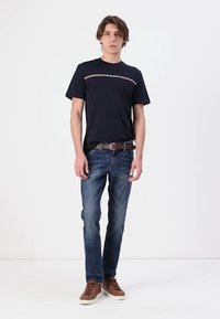 Marineblå crew neck t-skjorte med en hvit og rød horisontal stripe, kombinert med lyseblå denimjeans og brune sneakers. Enkelt, avslappet antrekk.